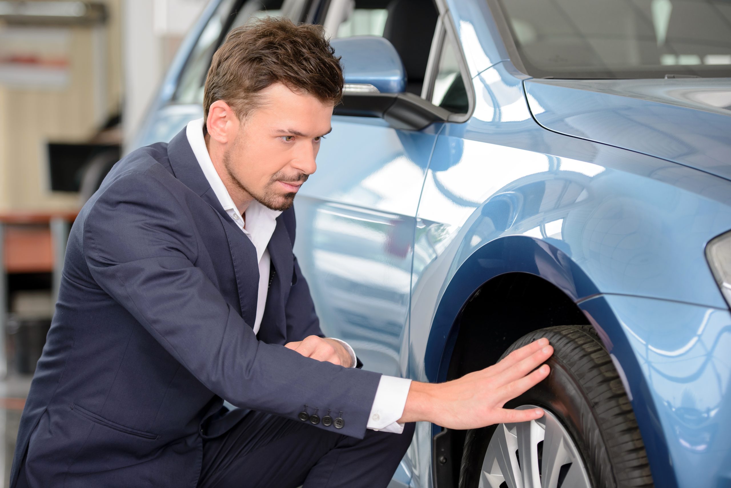 man in suit examining a used car's tire